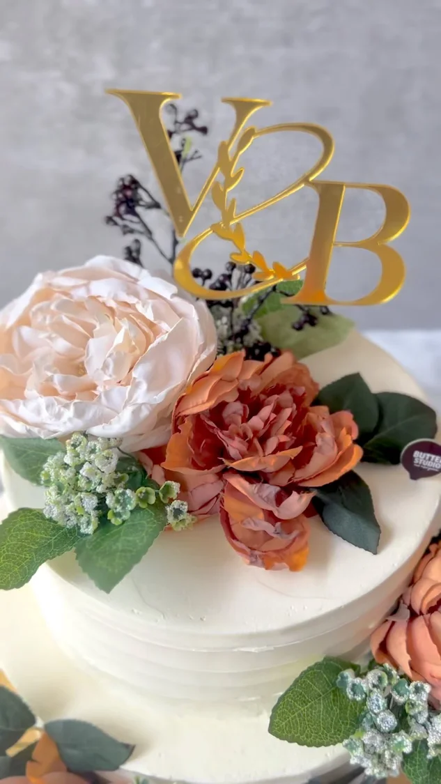 White cake decorated with pink roses and gold initials